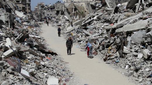 Palestinci procházejí kolem trosek domů a budov v severní části Pásma Gazy