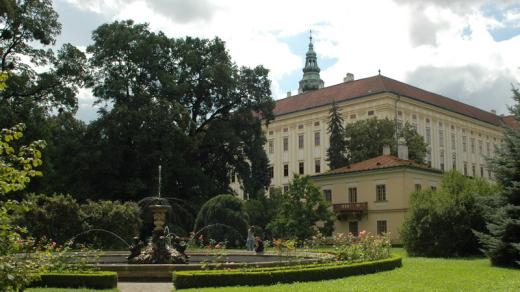 Pohled na Arcibiskupský zámek přes fontánu s vodní plochou a lekníny.