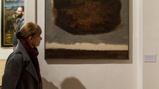 Žena si prohlíží obraz Kamila Linharta Kosmická kompozice 5. prosince 2019 v Severočeské galerii výtvarného umění v Litoměřicích na výstavě Minigalerie - Krajinou matematických her