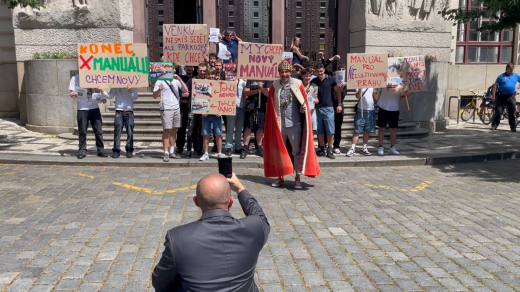 Šéf agentury Advertes fotí falešnou demonstraci. Několik účastníků drží bílý papír s QR kódem, který jim krátce předtím předal Leroy Weinrich a další pracovníci agentury