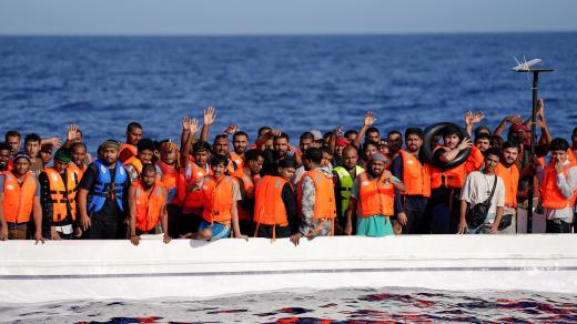 Migranti stojící na sklolaminátové lodi