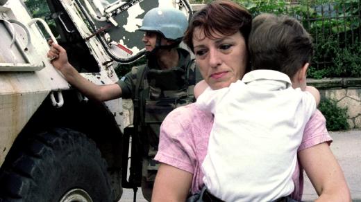 Žena drží své dítě a přenáší ho přes tzv. alej odstřelovačů v Sarajevu (1995)