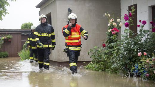 Hasiči procházejí kolem rodinného domu 29. června 2020 v Dolních Ředicích na Pardubicku, kde se kvůli silným dešťům vylil z břehů Ředický potok.