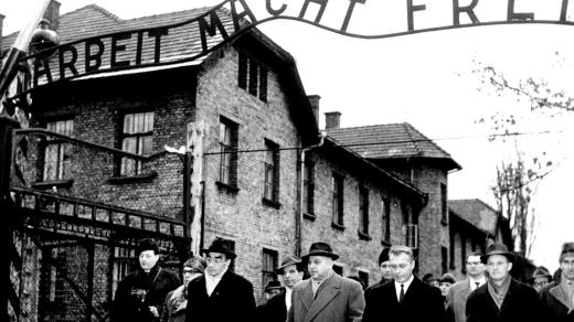 Členové frankfurtského soudu a novináři prochází branou osvětimského tábora s nápisem Arbeit macht frei (snímek z 14. prosince 1964)