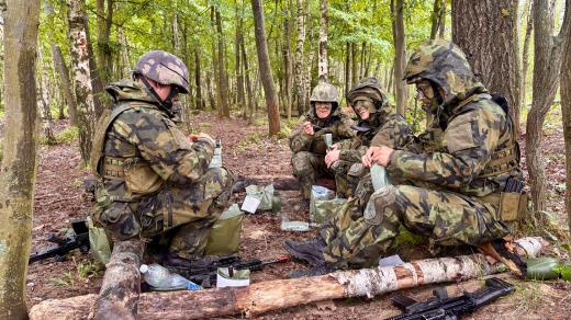 Družstvo rekrutů staví v listnatém lese ve výcvikovém prostoru Březina přístřešky