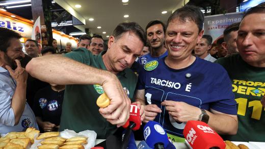 Flavio Bolsonaro během kampaně na trzích v Sao Paulu, když předstírá, že na novinářské mikrofony leje pálivou omáčku (28. září 2026)
