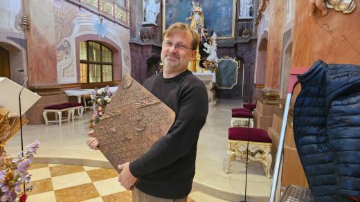 Farář Tomáš Holcner drží bronzovou desku se jmény 11 popravených