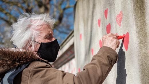 Senior s rouškou malující srdce