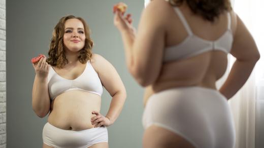 Sebevědomá plnoštíhlá žena se prohlíží v zrcadle a jí sladkou koblihu